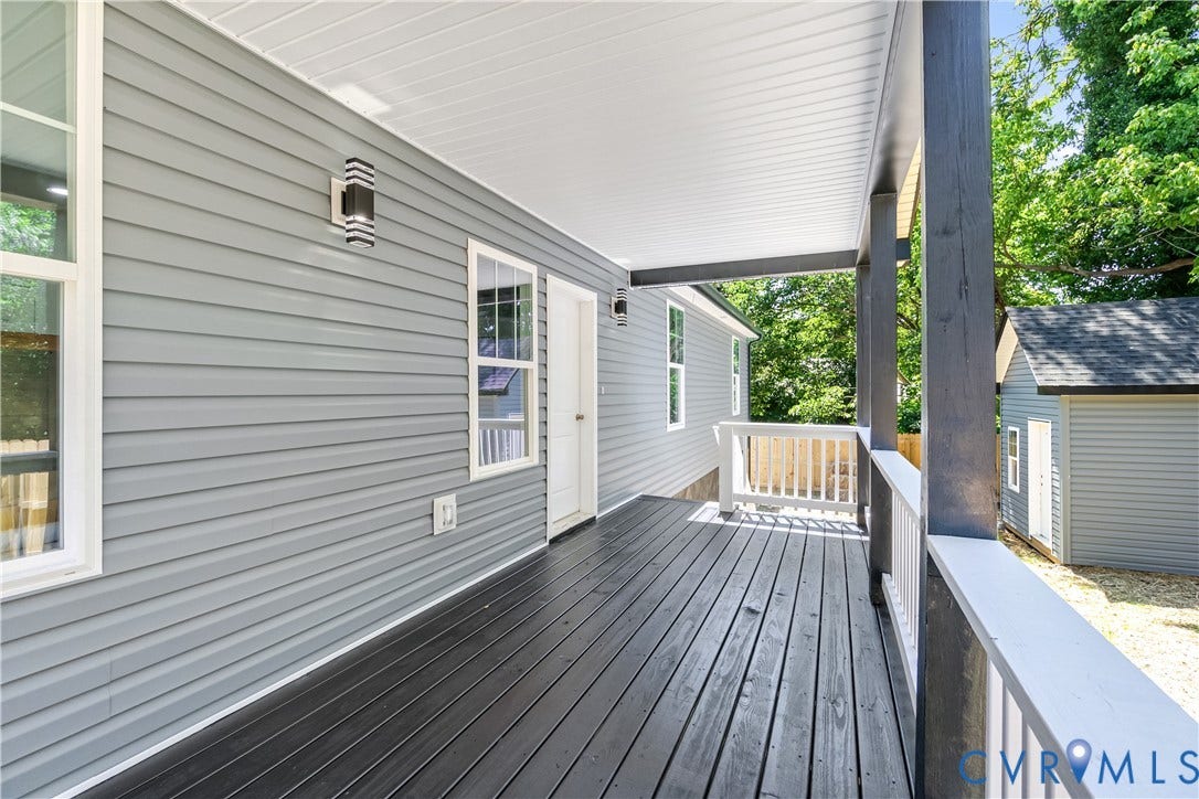 Covered porch featuring gray wood-finish decking, white railings, and gray siding