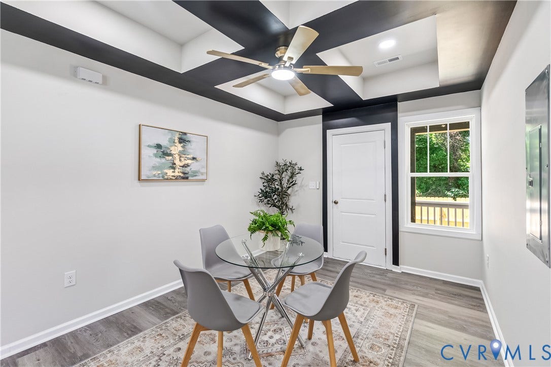 Tray ceiling with contrasting accents, ceiling fan with integrated lighting, wood-finish flooring, white paneled door, and a multi-pane window