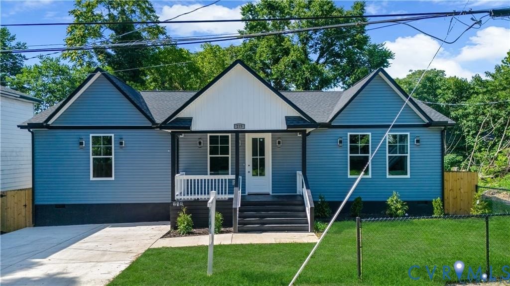 Single-story residence featuring blue siding with white and dark trim, a covered front porch with white railings, a concrete driveway, and a fenced front yard with a grass lawn