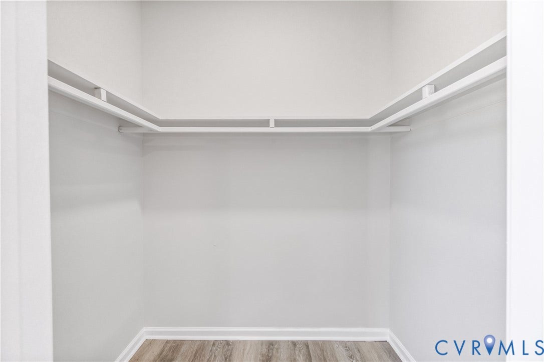 White painted walls, wood-finish flooring, and built-in shelving with hanging rod