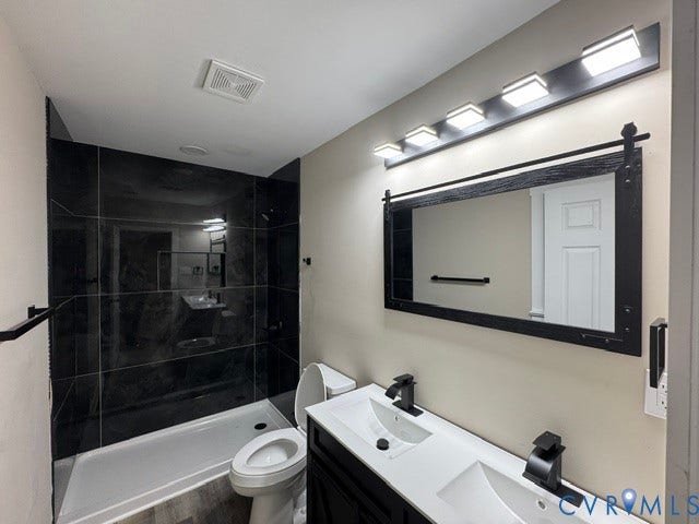 Dual vanity with integrated sinks and matte black fixtures, framed mirror with barn door hardware aesthetic, contemporary overhead lighting, and a tiled shower stall with a dark tile surround