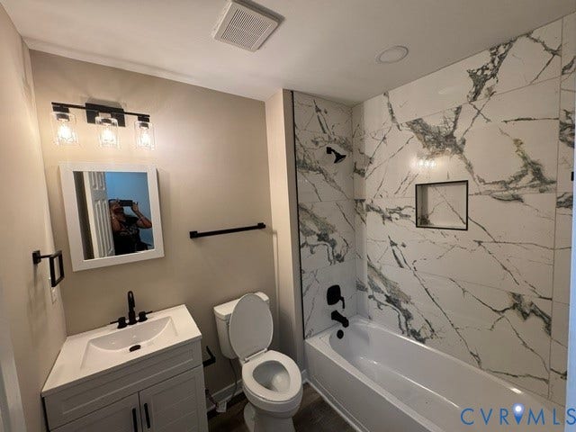 Bathroom featuring a white vanity with integrated sink, matte black fixtures, an illuminated mirror, a white bathtub, and large format wall tiling