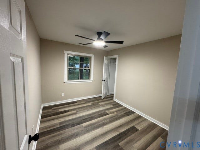 Wood-finish flooring, neutral wall tones, modern ceiling fan with integrated lighting, white trim accents, and a window with exterior views