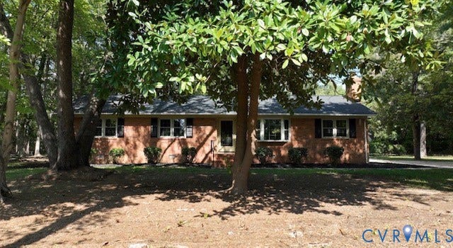 Brick exterior with a dark-shingled roof, featuring multiple windows with dark shutters, and a brick chimney