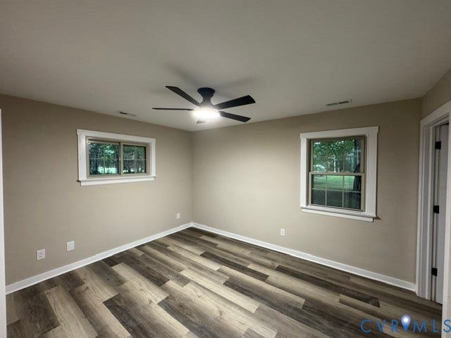 Wood-finish flooring, two windows with white trim, and a ceiling fan with integrated lighting