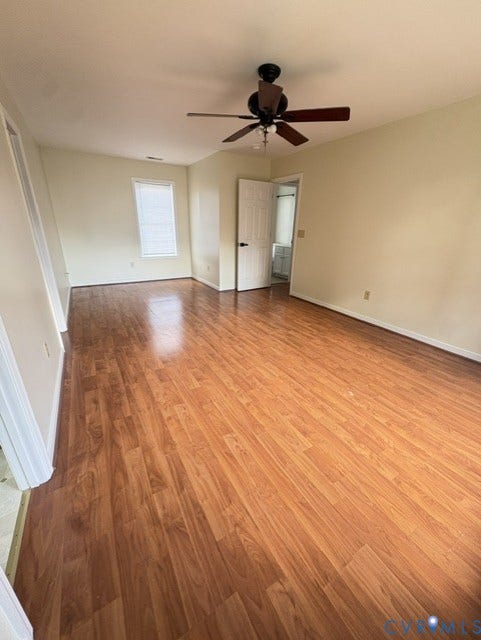 Spacious room featuring wood-finish flooring, light-toned wall paint, a ceiling fan with integrated lighting, and a window with blinds