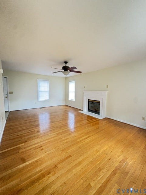 Hardwood flooring, white painted walls, fireplace with mantel, ceiling fan, and multiple windows