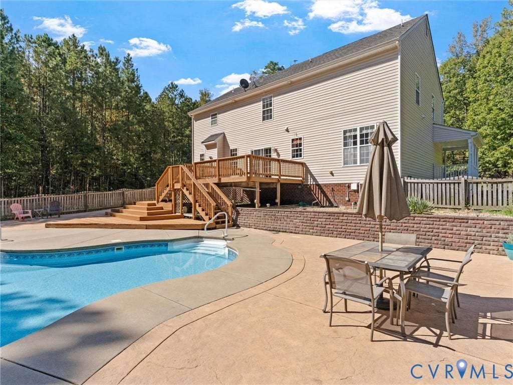 Rear exterior with a multi-level wood deck, an in-ground swimming pool, a concrete pool surround, and a brick retaining wall