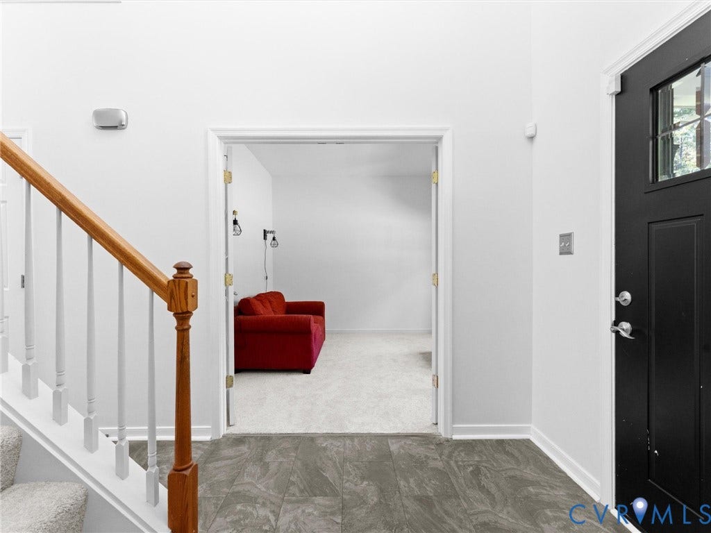 Entryway featuring dark gray tile flooring, a staircase with a wood handrail and white spindles, and a black front door with decorative glass inserts