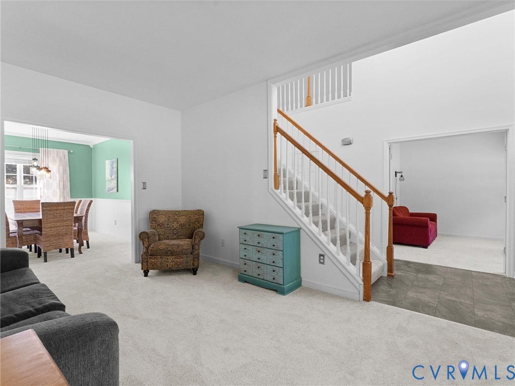 Carpeted living area with a white staircase featuring wood handrails and balusters