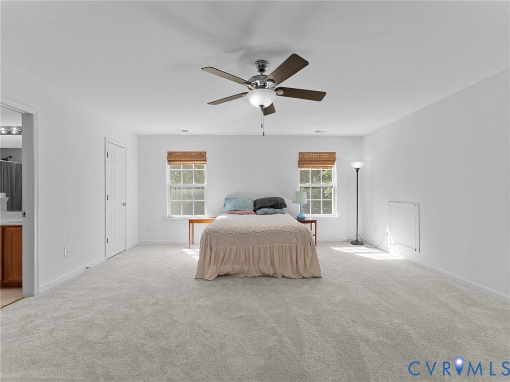 Spacious interior with neutral carpeting, a ceiling fan with integrated lighting, and two windows with blinds