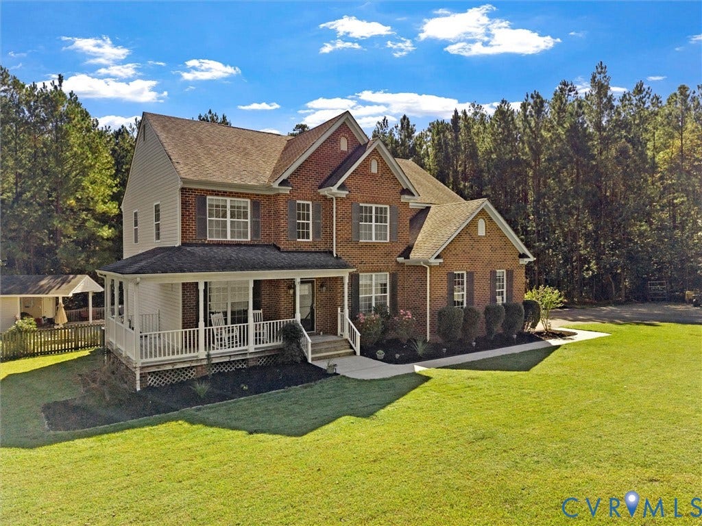 Brick and siding exterior with a covered front porch, an attached two-car garage, and mature landscaping
