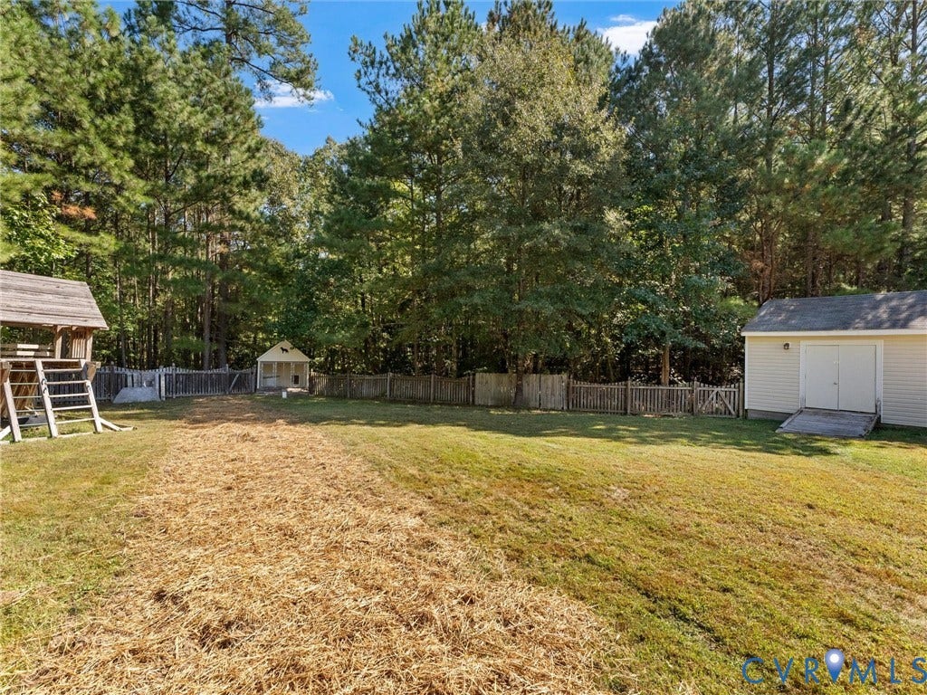 Expansive backyard featuring a privacy fence, mature trees, and an auxiliary storage shed