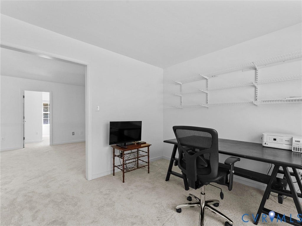 Light-toned wall-to-wall carpeting throughout, with a wide doorway offering access to an additional room
