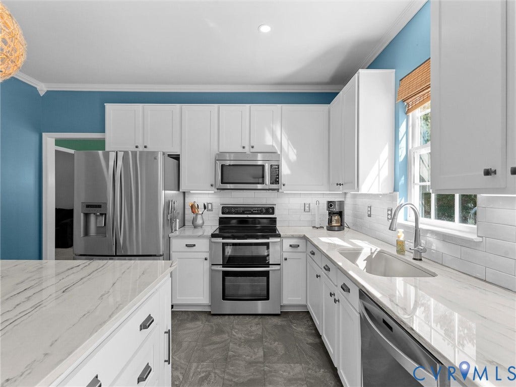 Kitchen featuring white cabinetry, stainless steel appliances, white subway tile backsplash, and light-toned countertops
