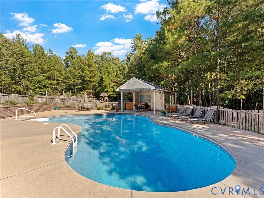 In-ground swimming pool with concrete surround, adjacent pool house, and surrounding privacy fencing