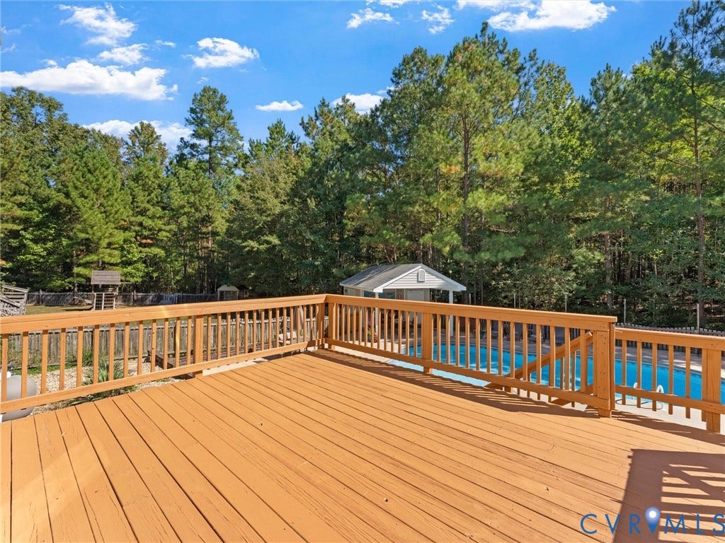 Spacious wood-finish deck with wood-finish railing, overlooking an in-ground pool and a secluded tree-lined perimeter