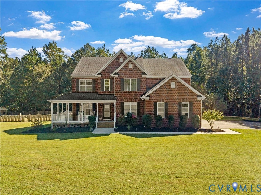 Two-story brick exterior, covered front porch, multi-pane windows with shutters, paved driveway, mature trees