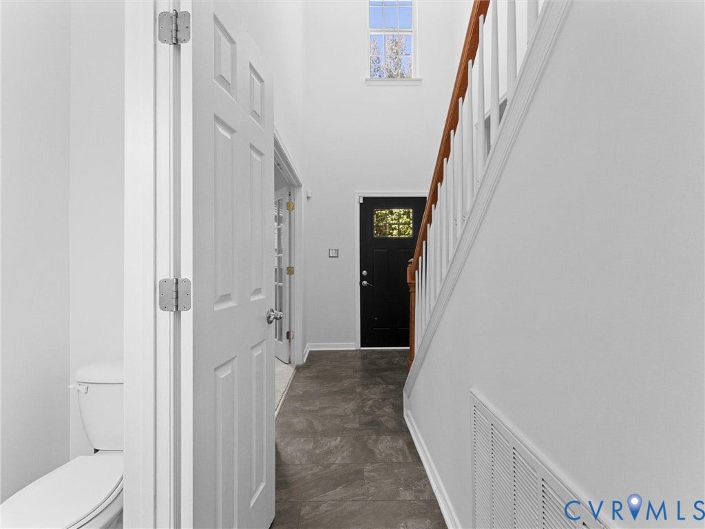Two-story entryway featuring a dark wood front door with decorative glass, a white spindle staircase with wood handrail, and gray tile flooring