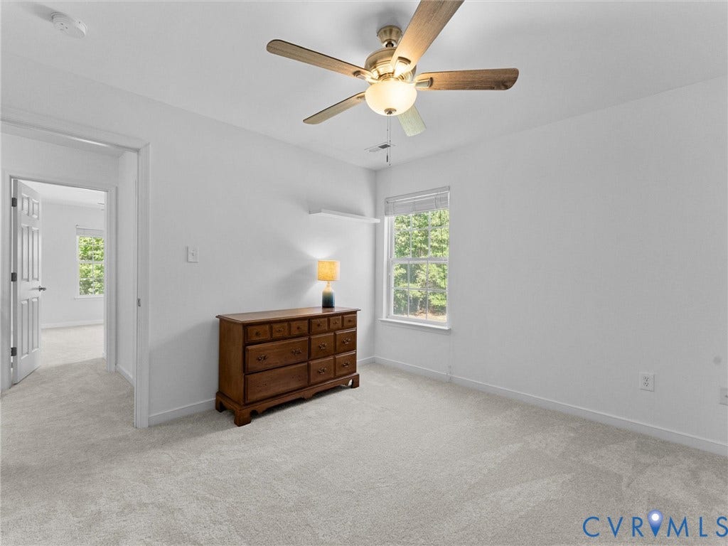 Soft gray carpeting, a window with blinds, and an overhead ceiling fan light fixture