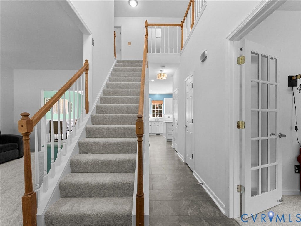 Two-story foyer featuring a carpeted staircase with wood handrails, white balusters, and a tiled hallway