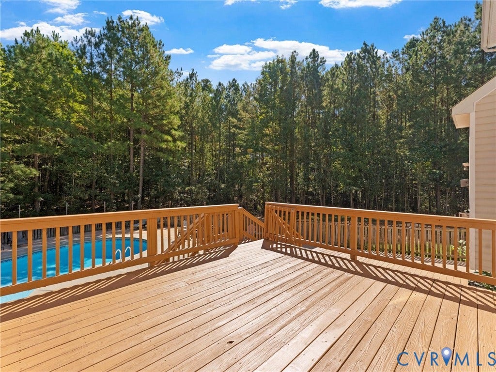 Expansive outdoor deck with wood-finish flooring, full railing, and integrated stairs, overlooking a swimming pool and mature trees