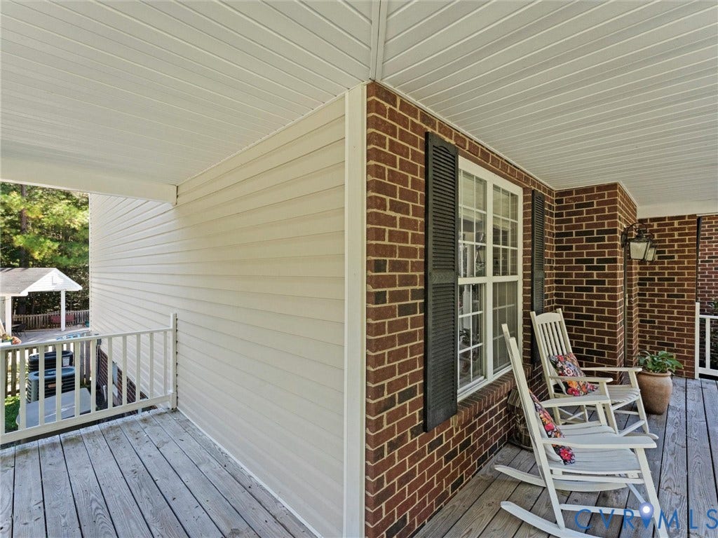 Covered porch featuring brick exterior, wood-finish decking, and white railing