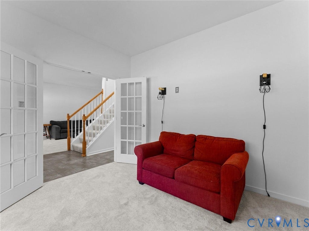 White French doors, light gray wall-to-wall carpeting, and a staircase with wood railings