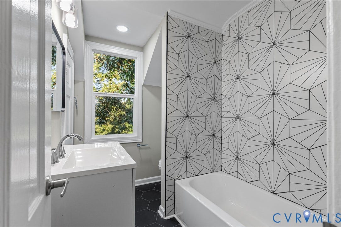 2606 Hawthorne Avenue, Richmond, VA 23222 White vanity with an integrated sink and chrome faucet, hexagonal floor tiling, and patterned wall tile surrounding the bathtub