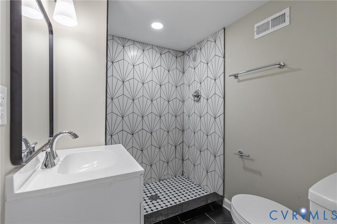 2606 Hawthorne Avenue, Richmond, VA 23222 Contemporary bathroom featuring a walk-in shower with geometric tile, white vanity with integrated sink, chrome fixtures, and dark hexagonal floor tiles