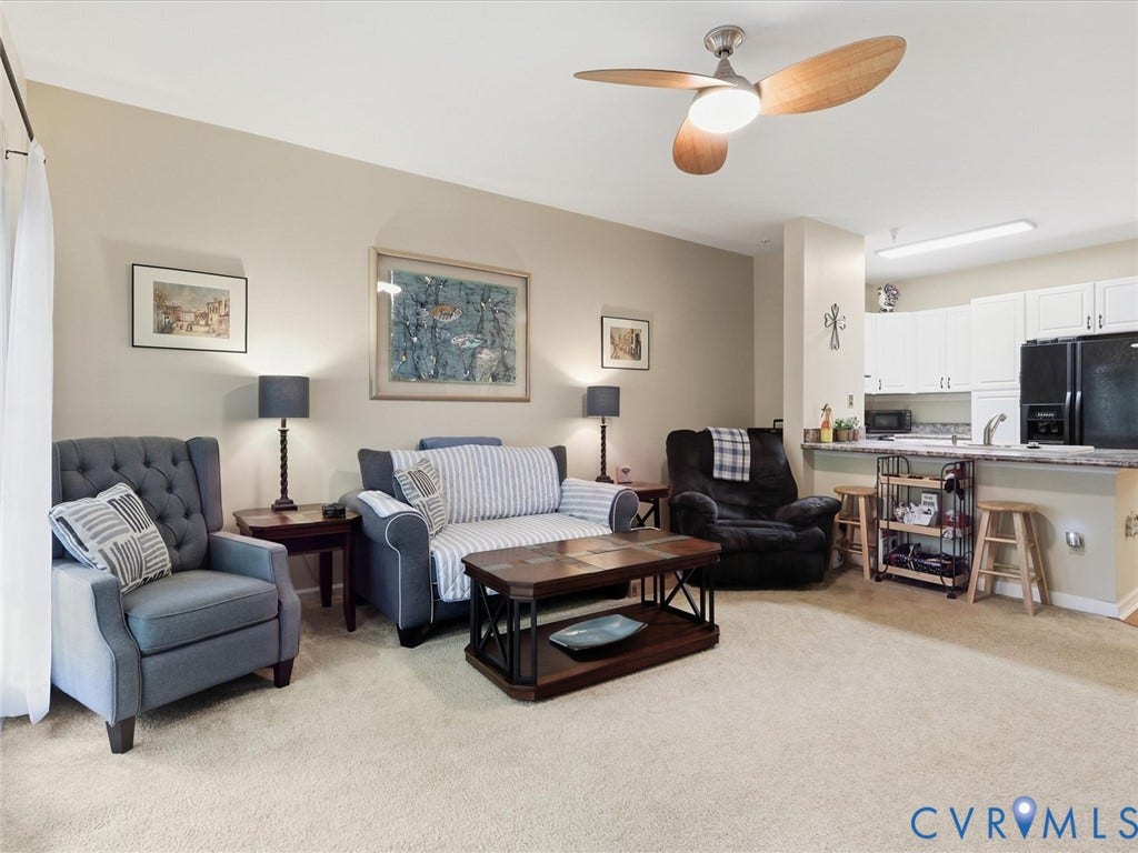 Open-concept living space featuring a ceiling fan, carpeted flooring, and an integrated kitchen with white cabinetry, a black refrigerator, and a breakfast bar