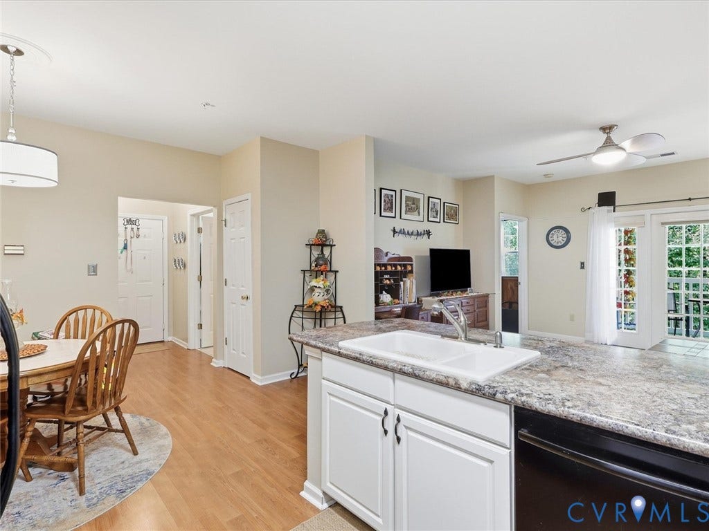 Kitchen with white cabinetry, a double basin sink, and a dishwasher, opening to a dining area with wood-finish flooring
