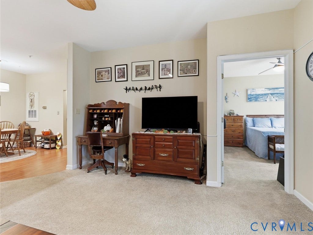 Carpeted living area with a ceiling fan and an open doorway to a bedroom