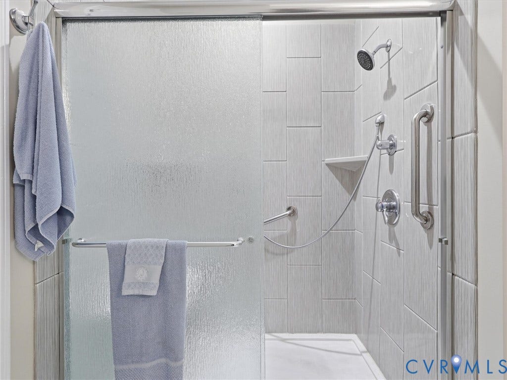 Shower enclosure with frosted glass sliding doors, textured tile surround, and built-in grab bars