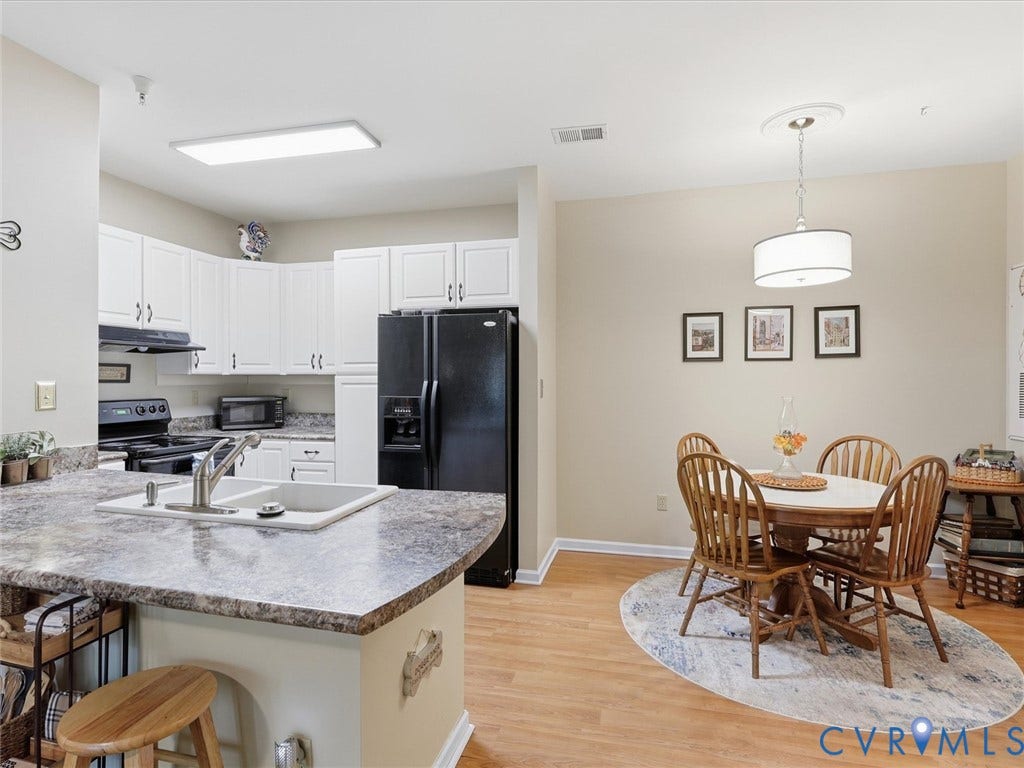 Kitchen featuring white cabinetry, a black appliance package, laminate flooring, and a breakfast bar with a double basin sink