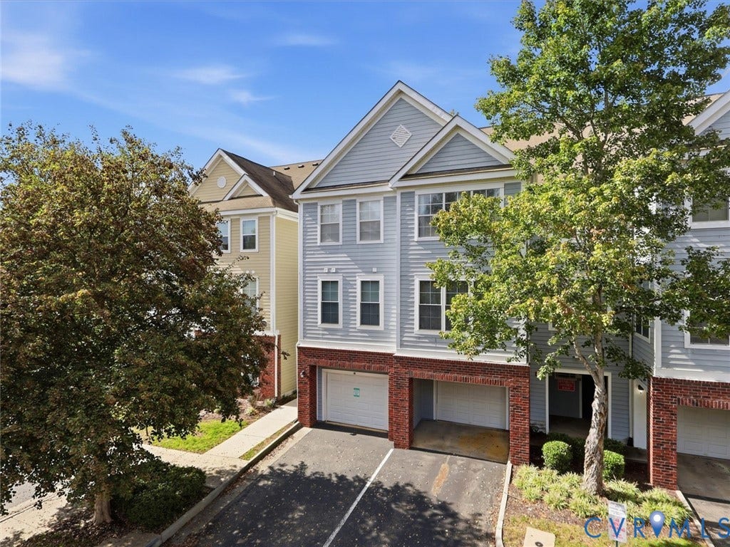 Three-story townhouse featuring light blue siding, brick foundation, and an attached garage