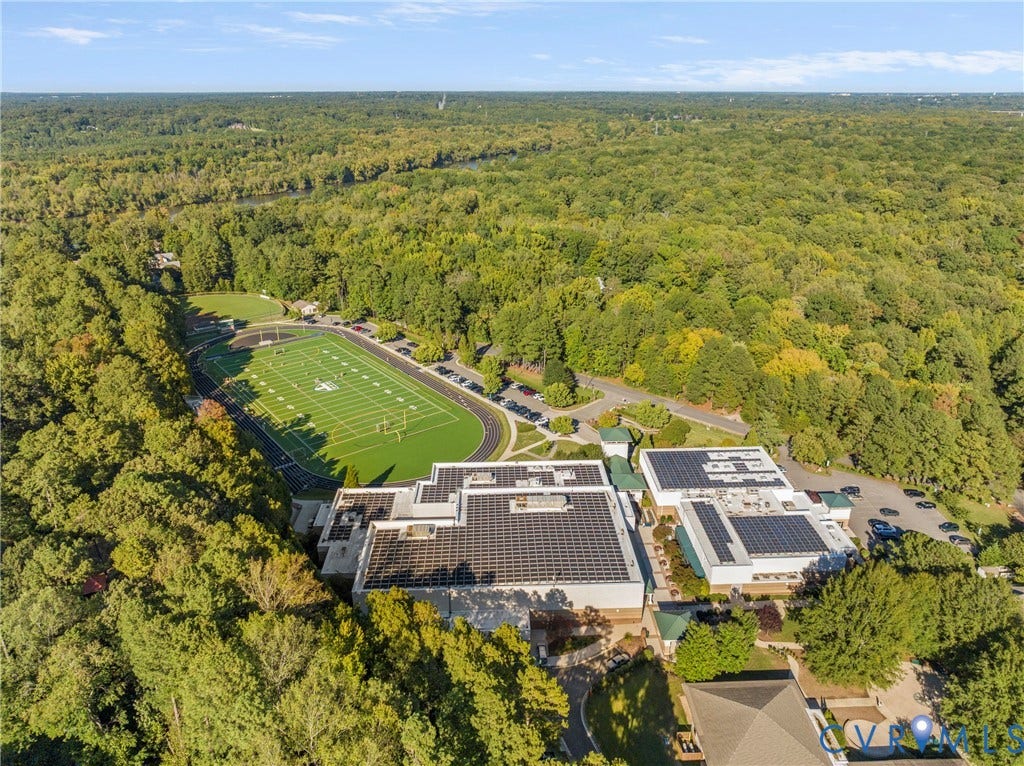 Extensive wooded surroundings, large building structures, multiple solar panel installations, dedicated sports field, and paved parking areas