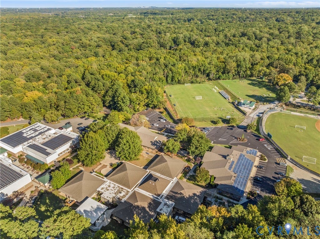 Expansive wooded surroundings, multiple buildings with solar panel arrays, manicured sports fields, and a baseball diamond