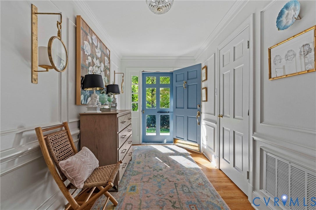 Hardwood flooring, paneled walls, crown molding, a decorative ceiling fixture, and a blue front door