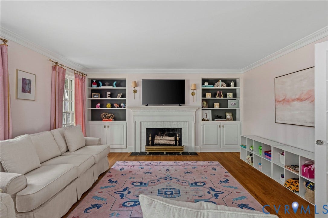 Hardwood flooring, crown molding, built-in shelving, built-in cabinetry, and a fireplace with a mantel
