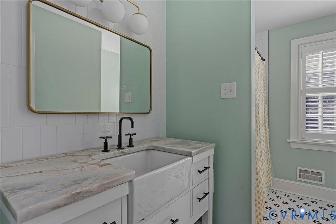 White vanity with black hardware, farmhouse sink, stone countertop, matte black faucet, and a gold-framed mirror