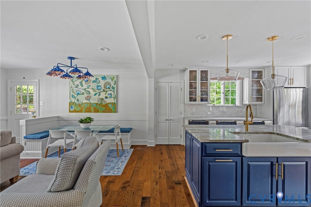 Open-concept living area with wood-finish flooring, a kitchen island featuring a farmhouse sink, and a built-in banquette dining space