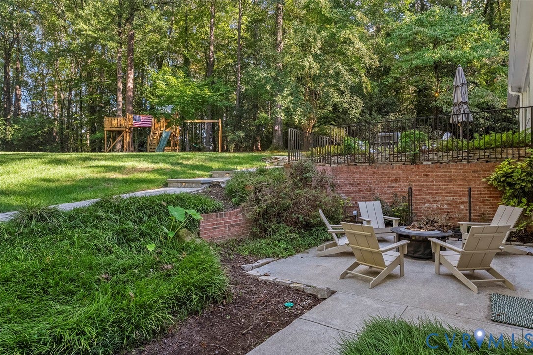 Expansive backyard with a concrete patio, brick retaining wall, and a raised lawn area