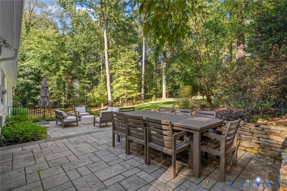 Expansive stone paver patio featuring a stacked stone wall and lush perimeter landscaping