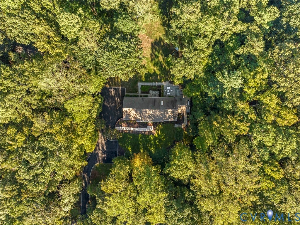 Secluded property surrounded by mature trees, featuring a private driveway, a residence with a dark roof, and an outdoor patio space