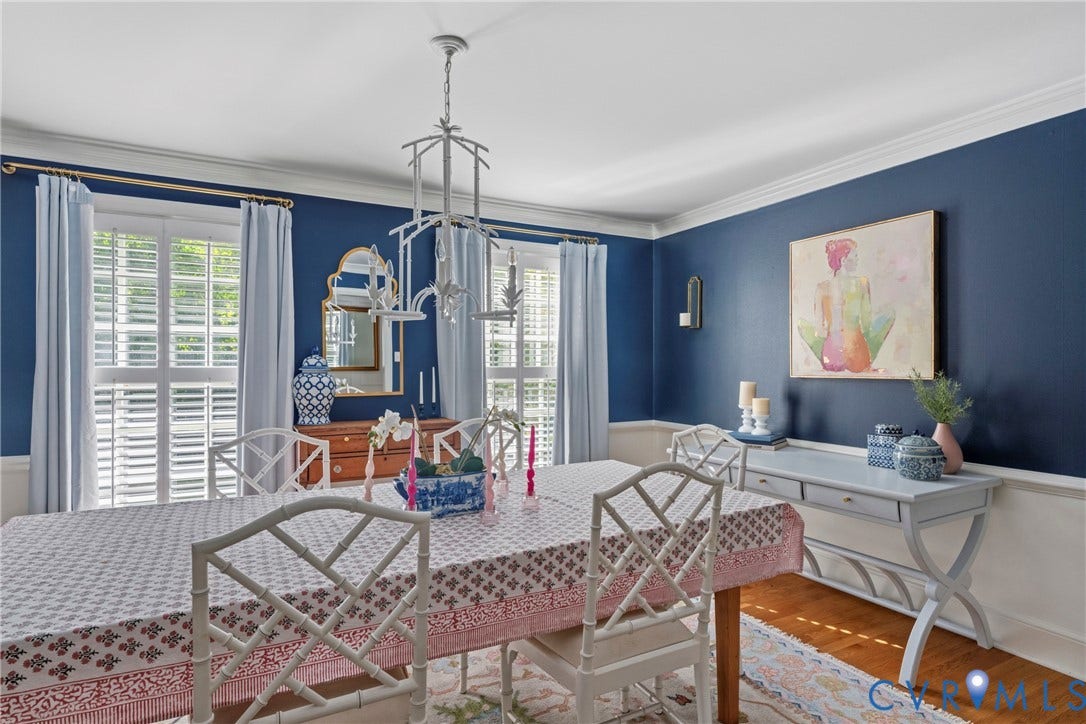 Crown molding, wood-finish flooring, white window shutters, and a central chandelier
