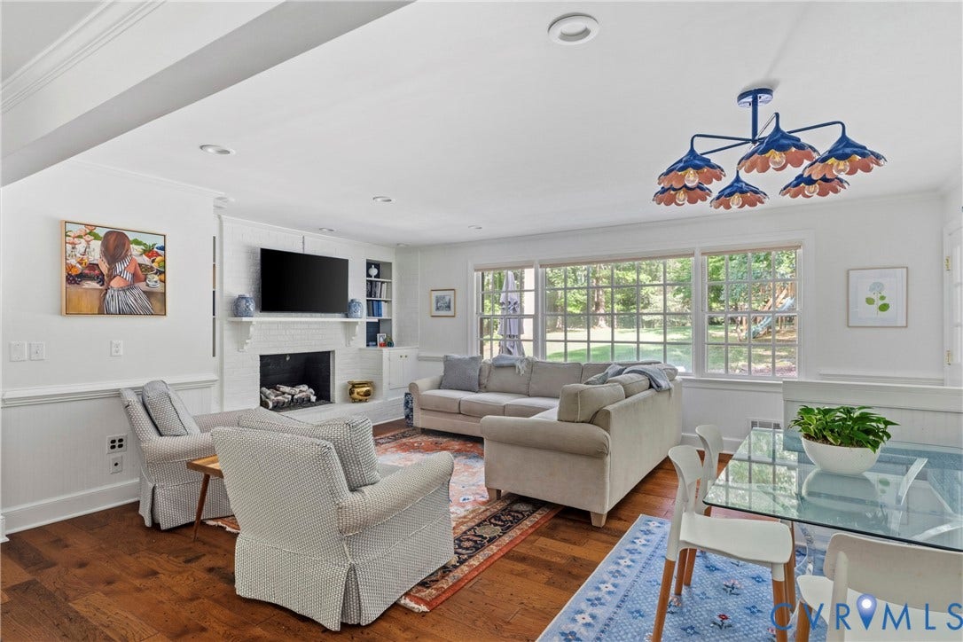 Wood-finish flooring, white brick fireplace with built-in shelving, recessed lighting, large multi-pane windows, and a distinctive ceiling fixture