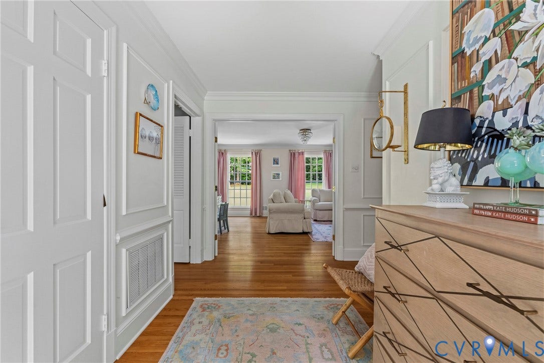 Hardwood flooring throughout, white paneled walls, crown molding, and a paneled interior door