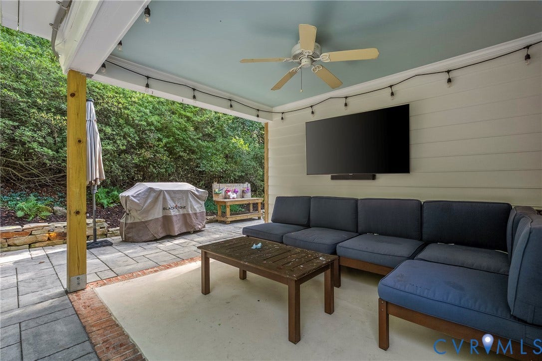 Covered patio with a mounted television, ceiling fan, string lighting, and shiplap-style wall