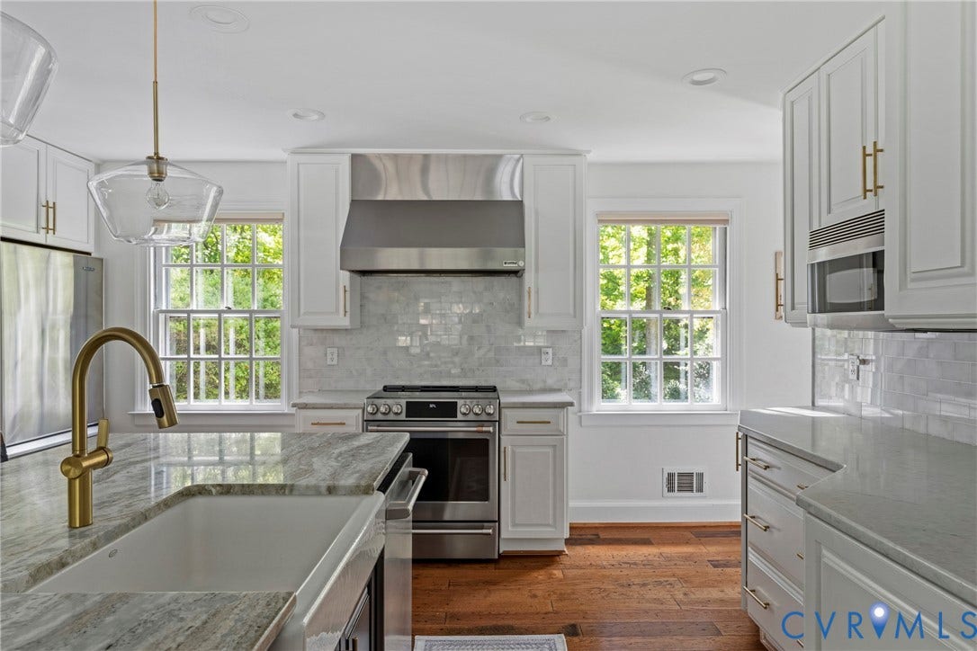 Kitchen featuring white cabinetry with gold-toned hardware, stainless steel appliances, a brass-finish faucet, and light-toned countertops